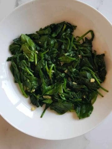 Garlic sauteed spinach in a bowl on a marble table.