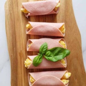 Ham, egg and cheese rollups on a wooden board.