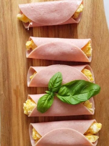 Ham, egg and cheese rollups on a wooden board.