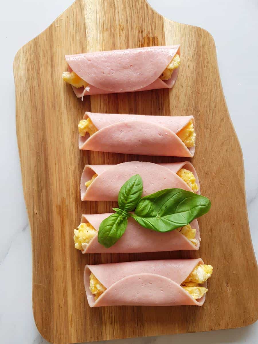 Ham egg and cheese rollups on a wooden board.