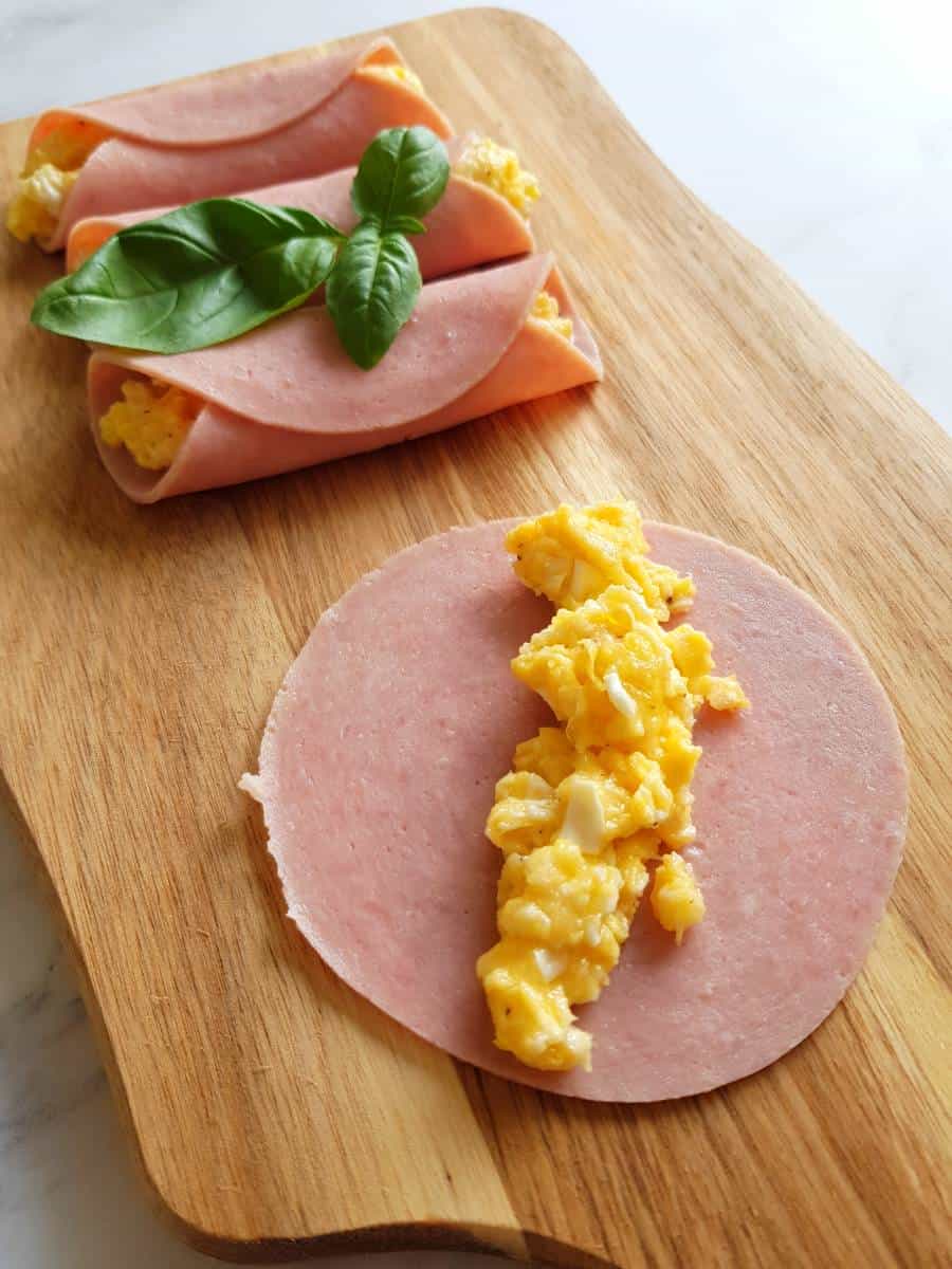 Ham roll ups with scrambled eggs on a chopping board.