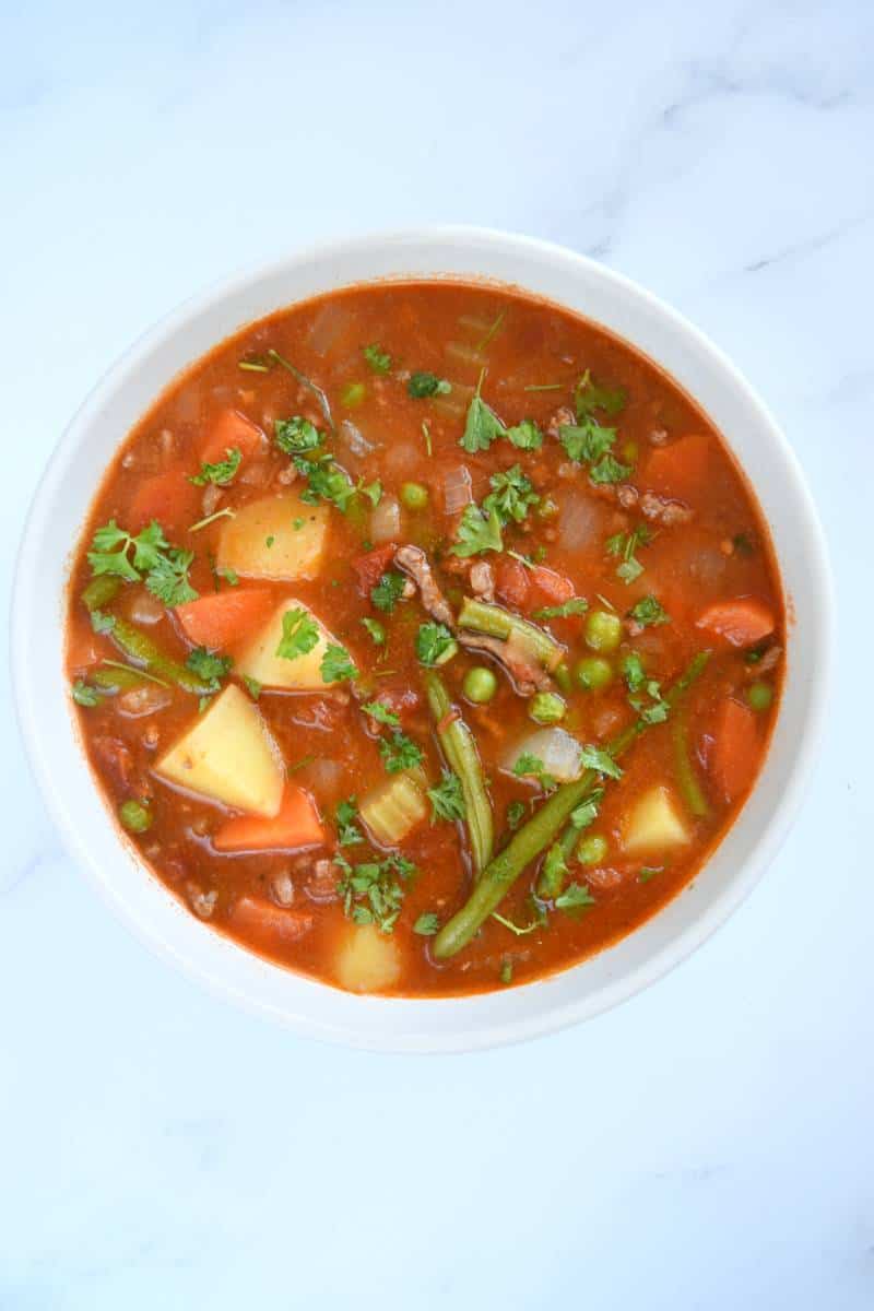 Hamburger soup in a white bowl on a marble table.