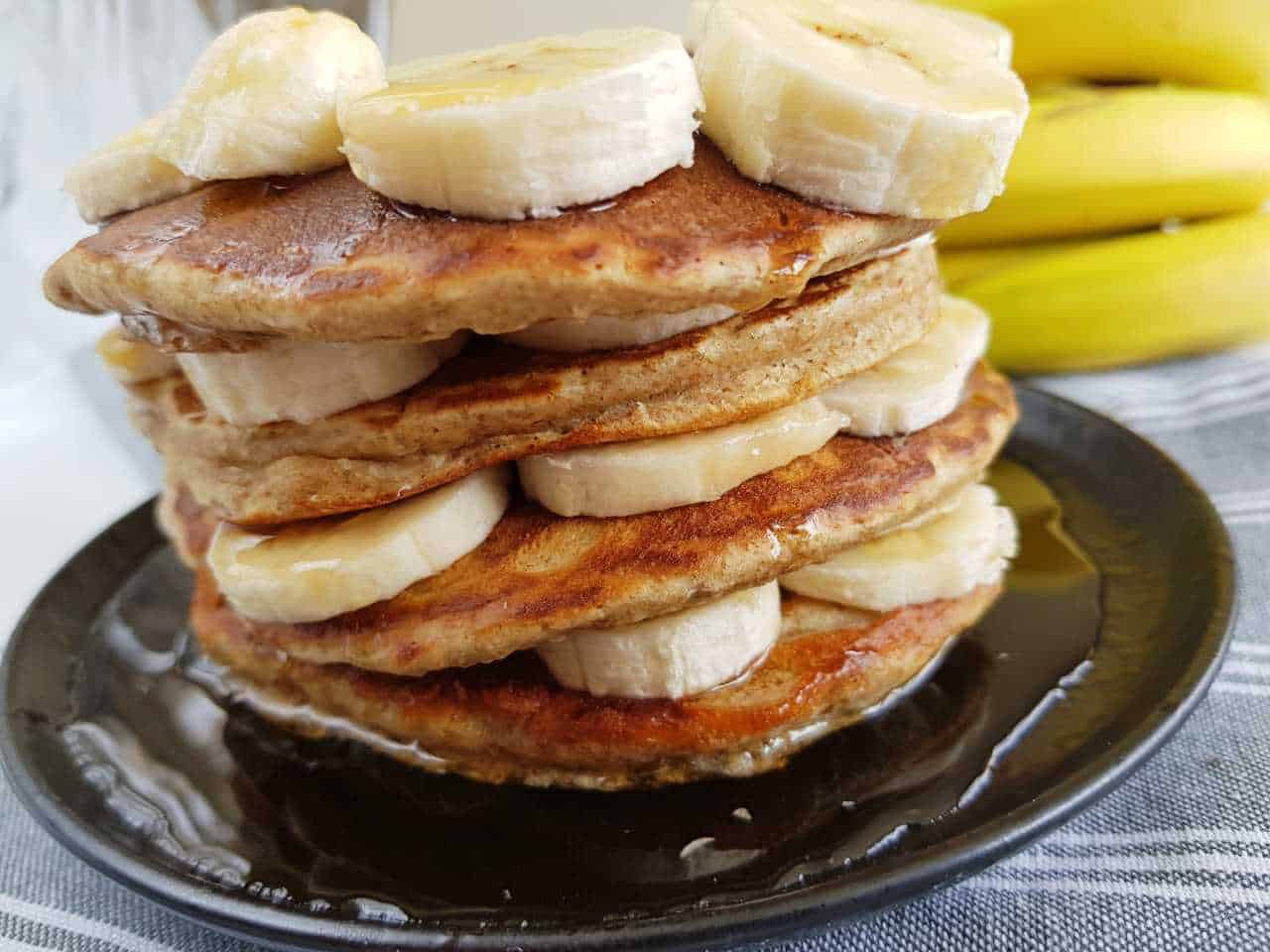 Banana pancakes stacked with sliced bananas on a plate.