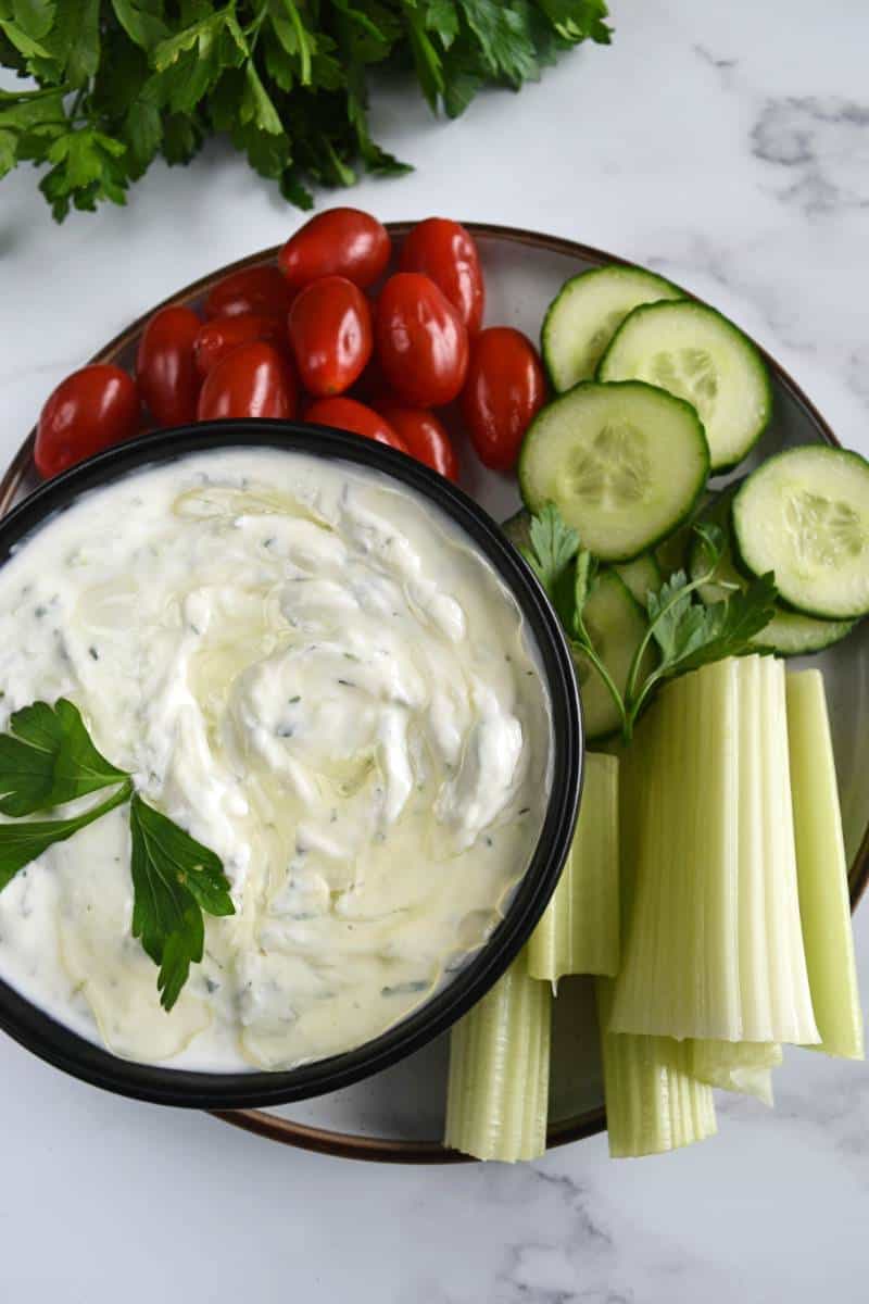 Homemade tzatziki sauce in a bowl with fresh parsley, tomatoes, cucumber and celery.