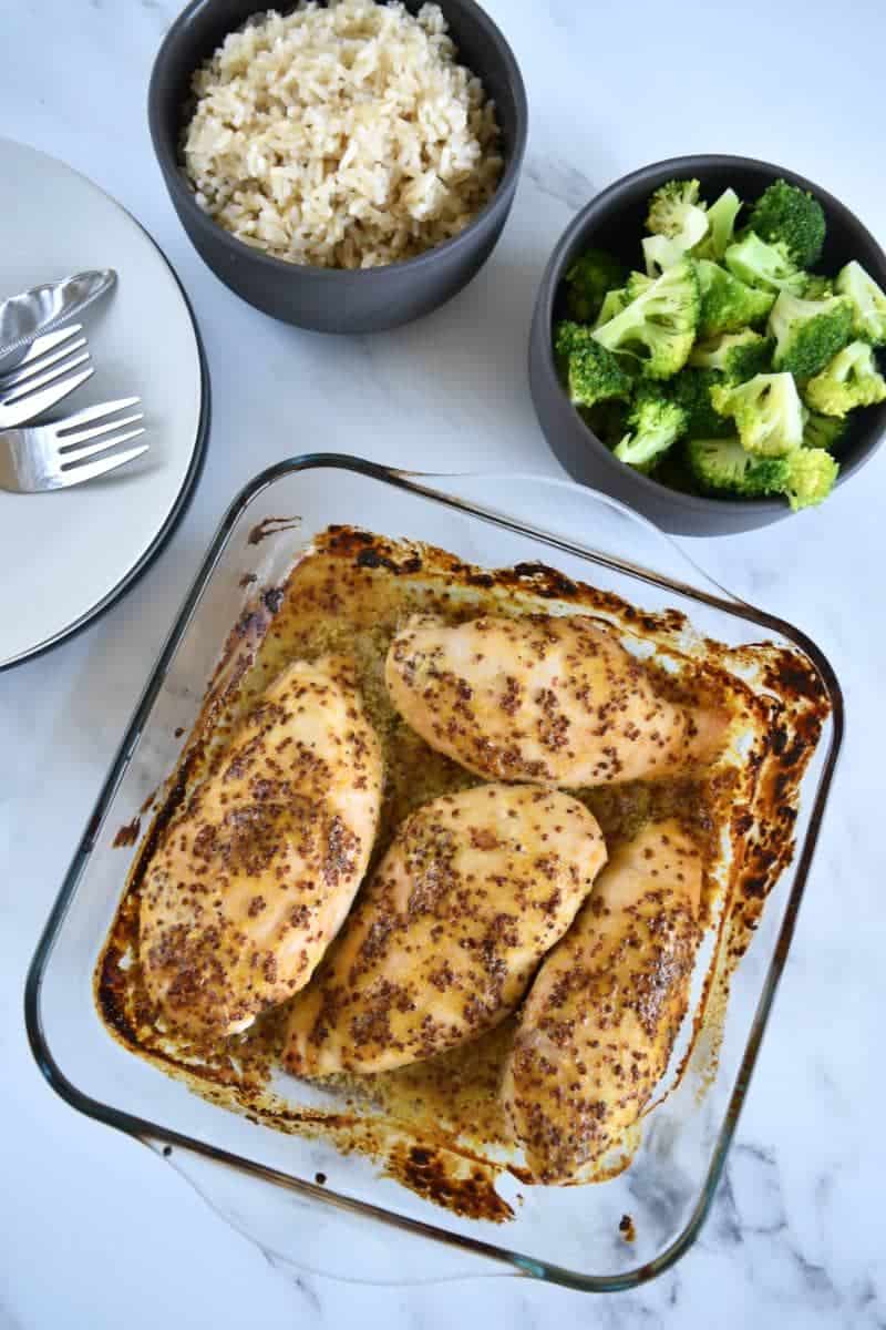 Sweet mustard chicken in a baking dish, surrounded with side dishes and plates.