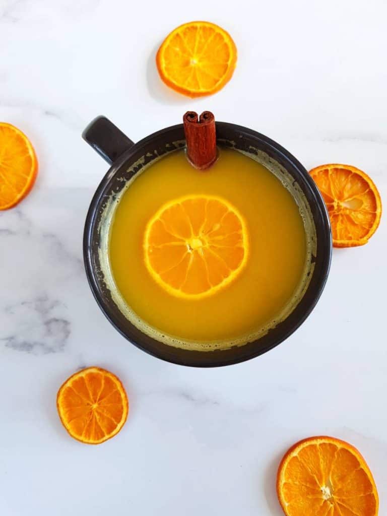 Hot orange juice in a cup surrounded by dried orange slices.