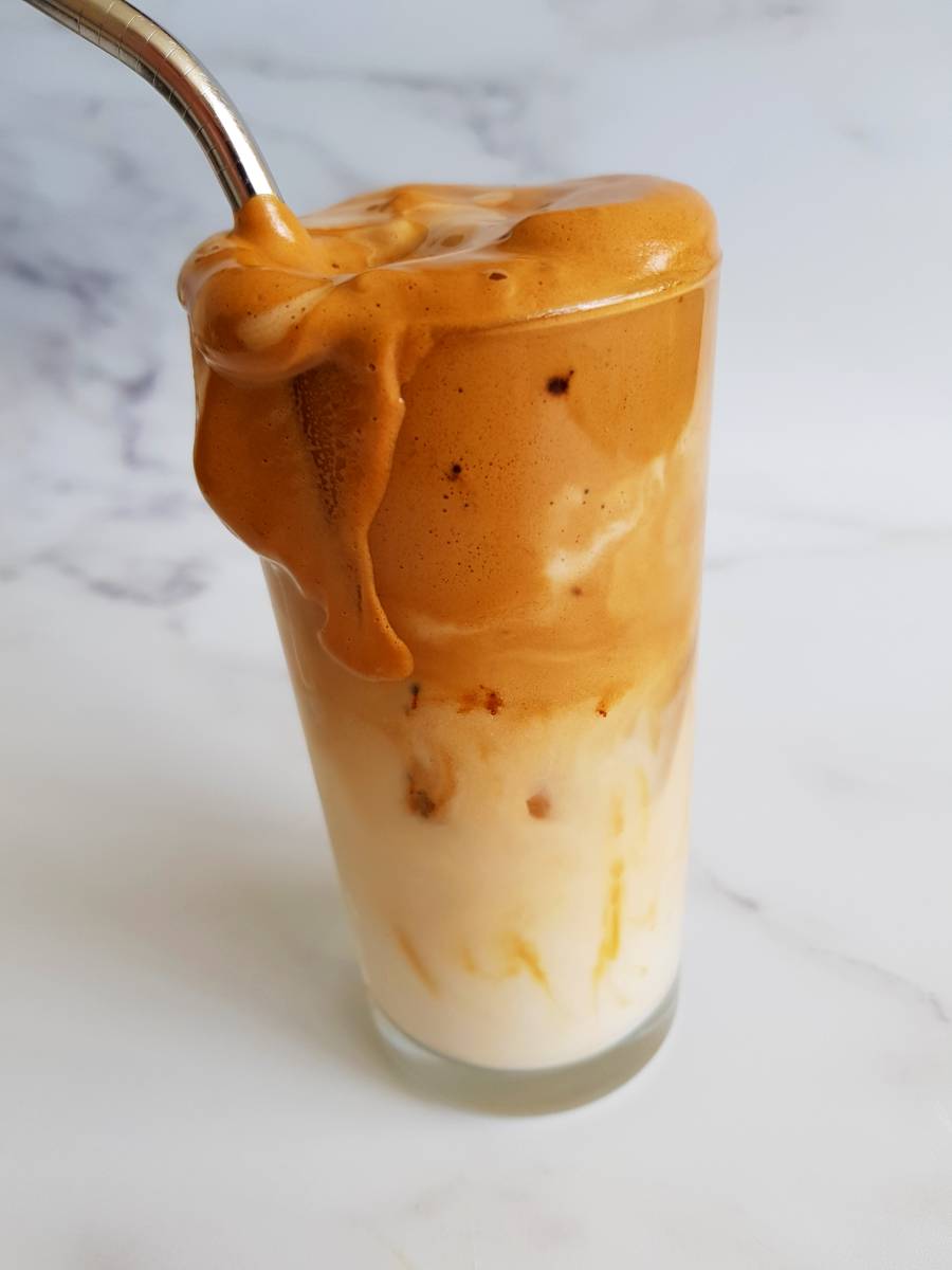 Iced whipped coffee with almond milk in a glass with a metal straw.