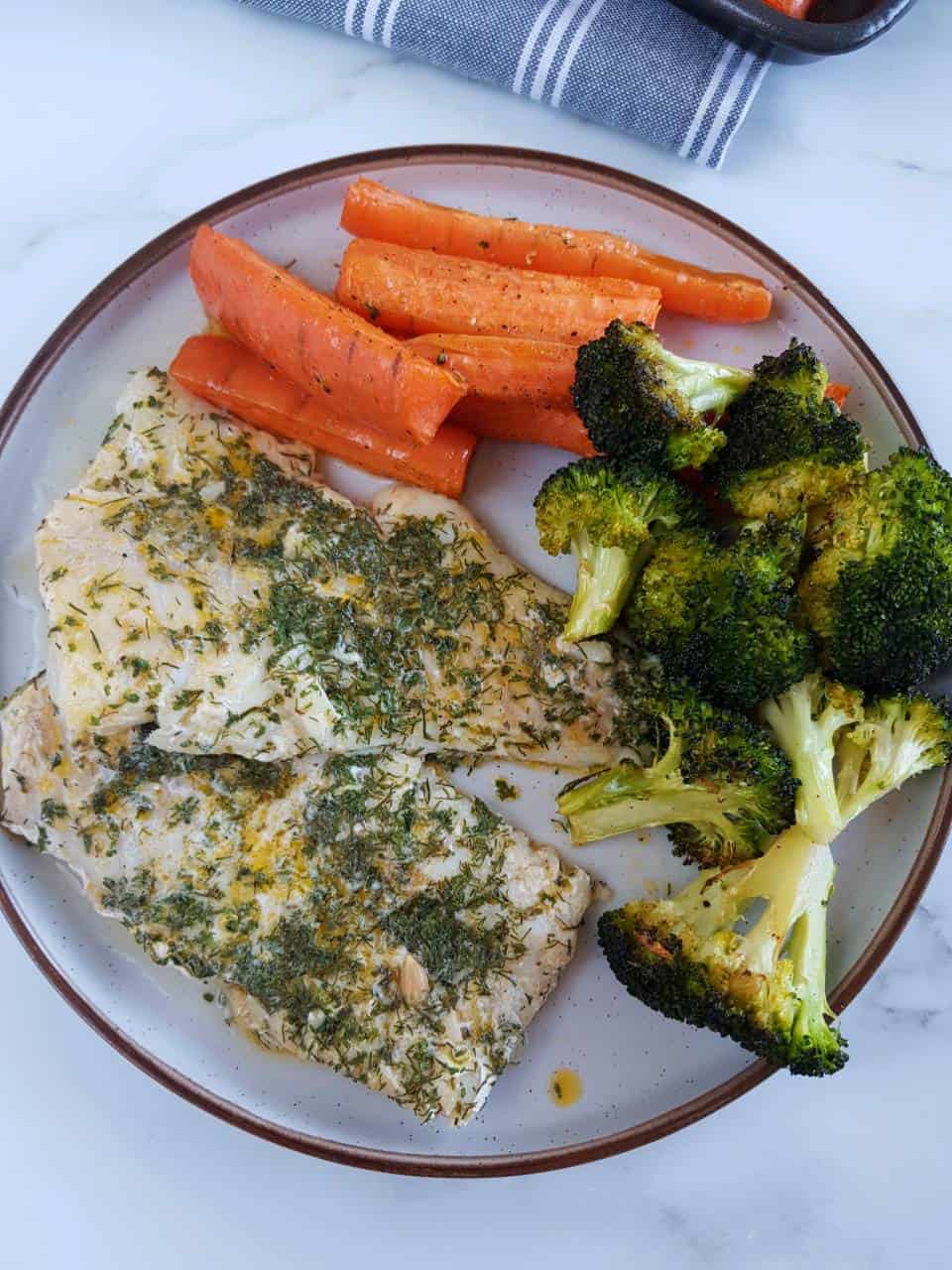 Herbed cod on a plate with roasted broccoli and carrots.