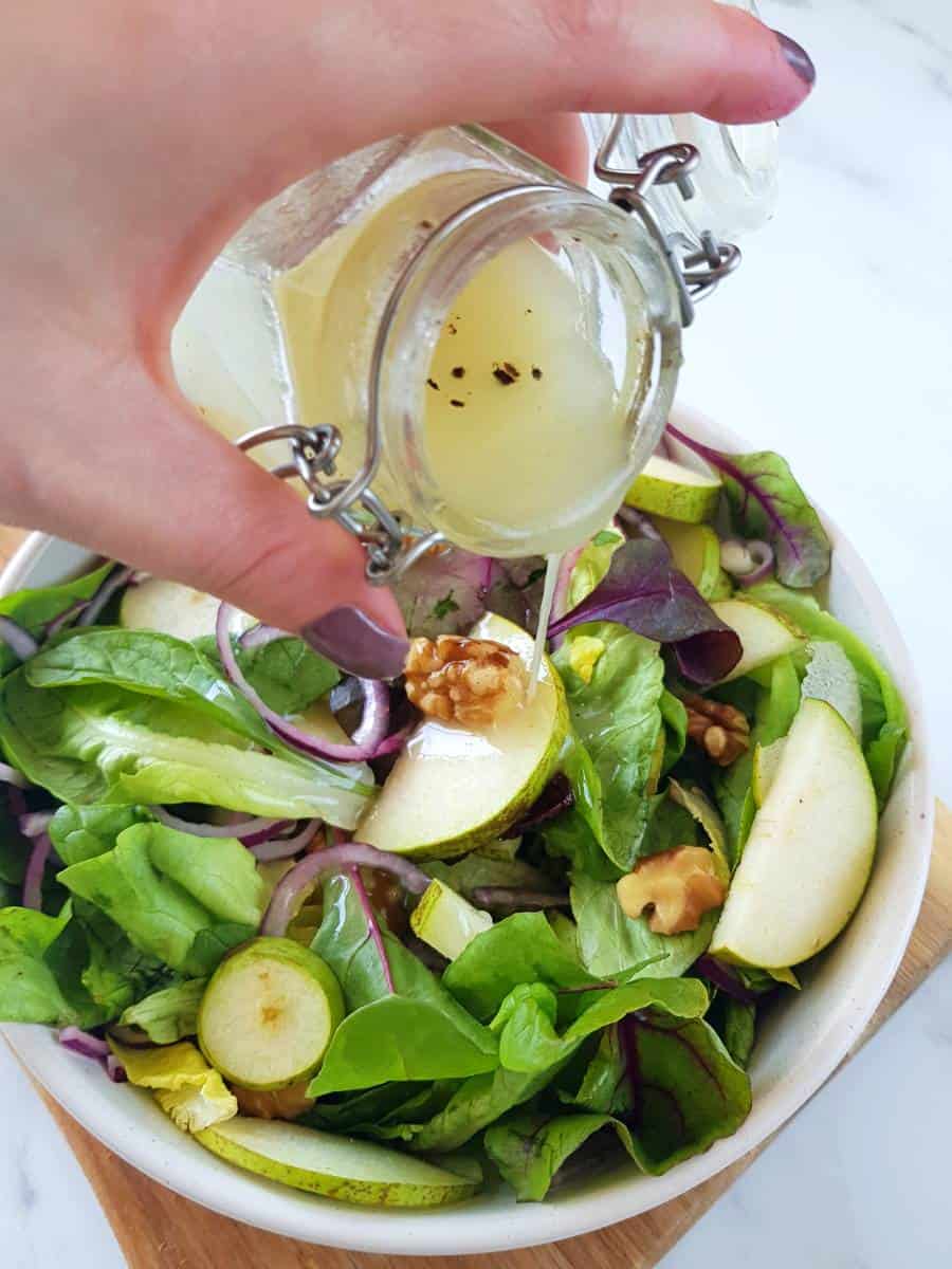 Pouring lemon pepper vinaigrette over a salad.