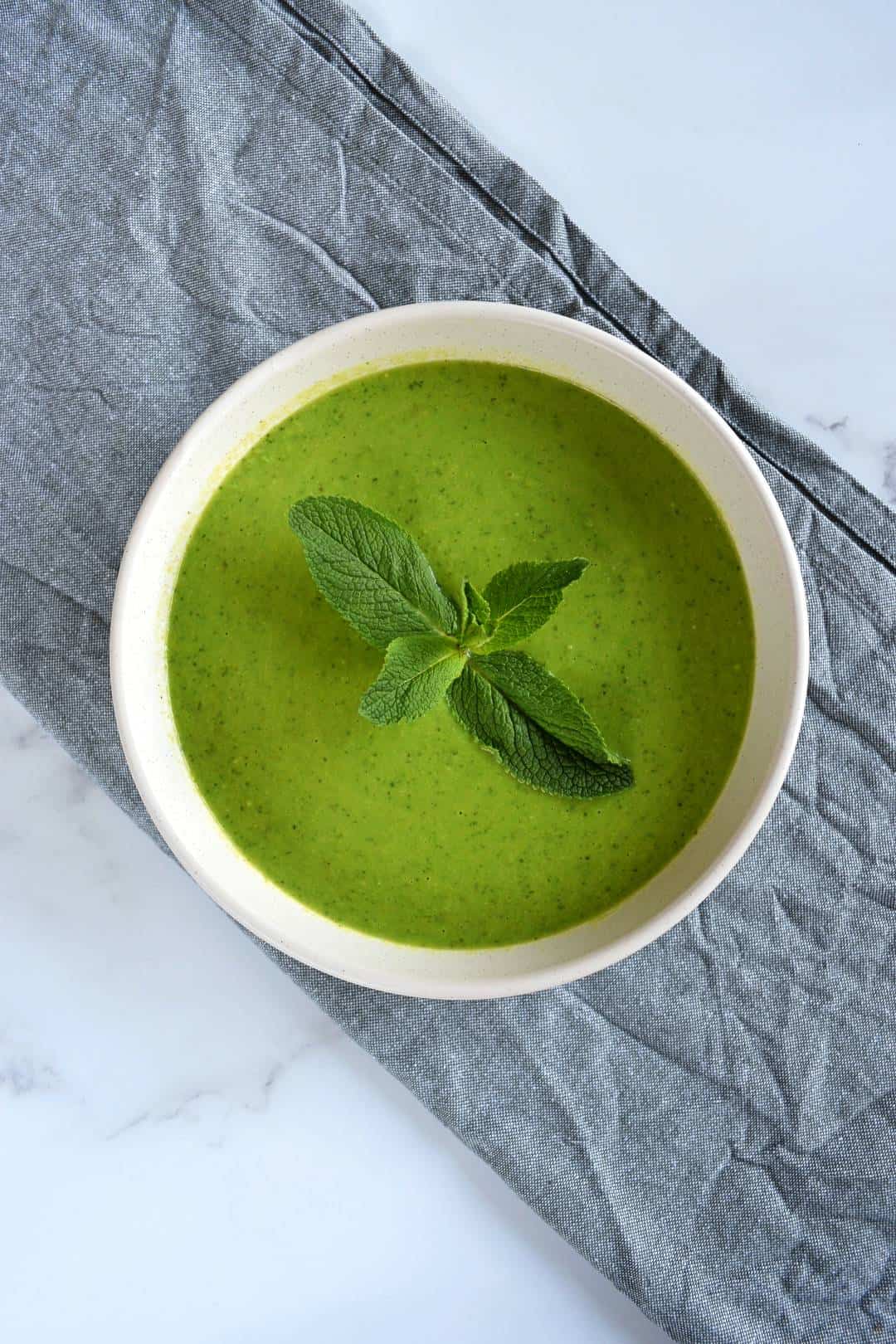 Minty pea soup in a white bowl with a sprig of mint on top.