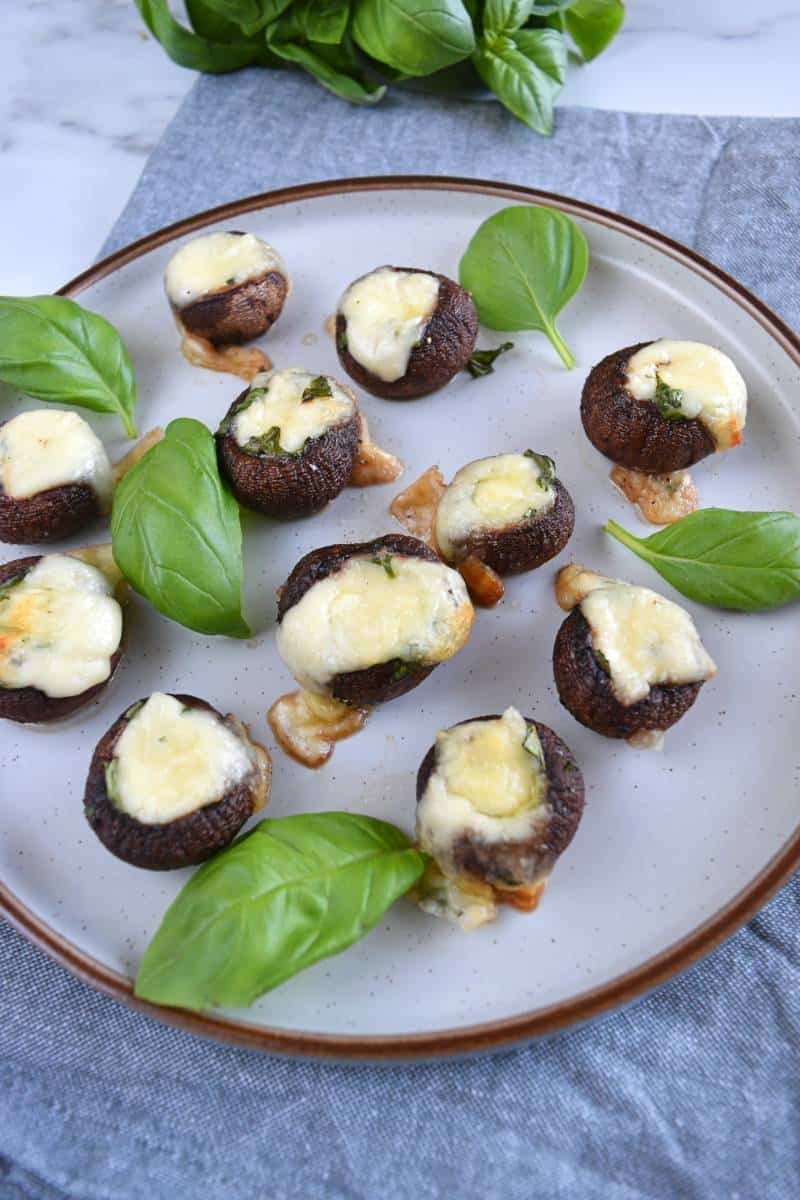 Mozzarella stuffed mushrooms on a plate with fresh basil.