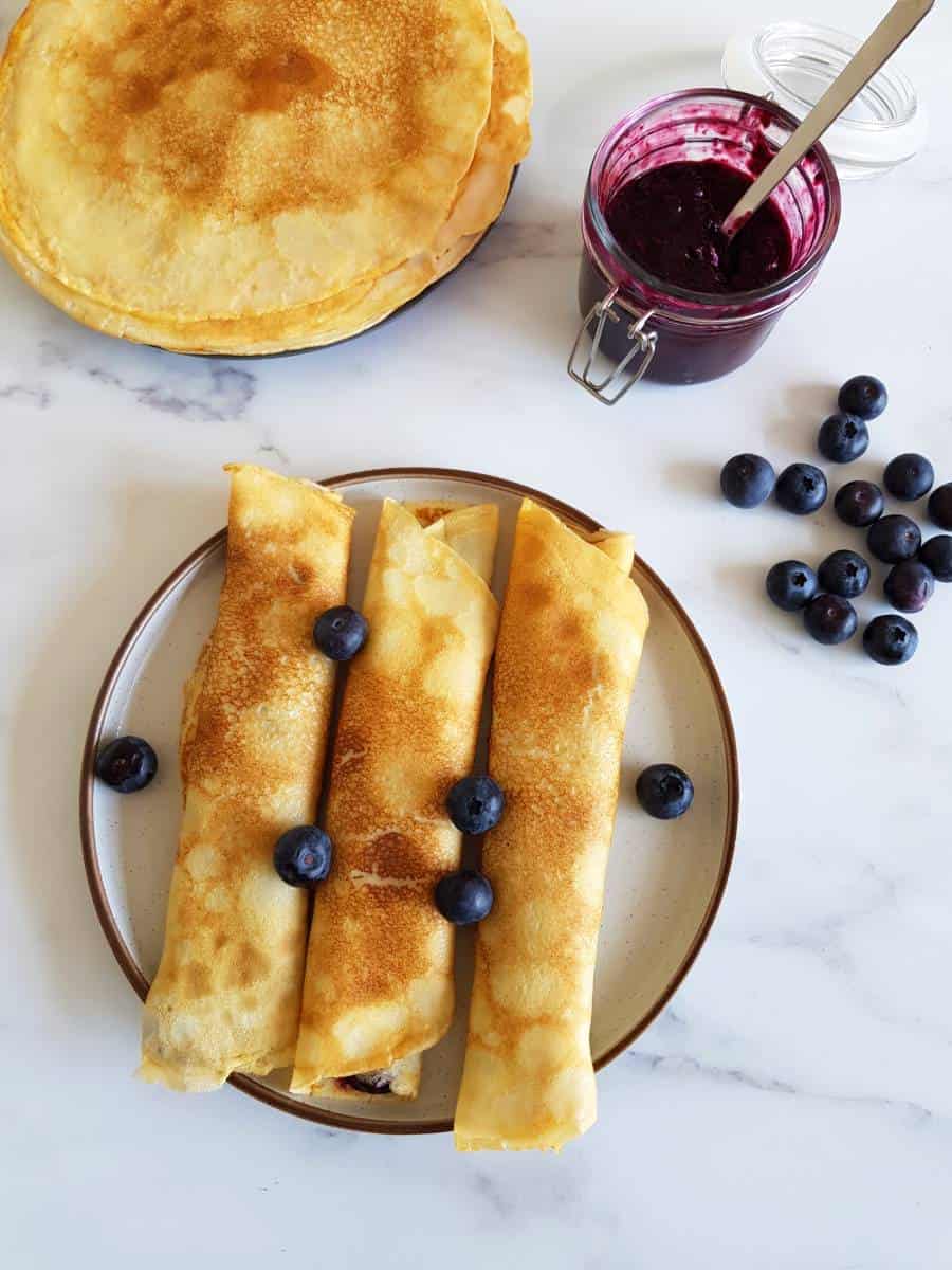 Norwegian pancakes filled with blueberry jam and blueberries on the side.