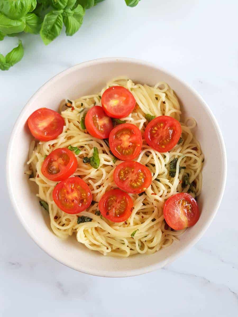 Noodles com manjericão e tomate numa tigela.