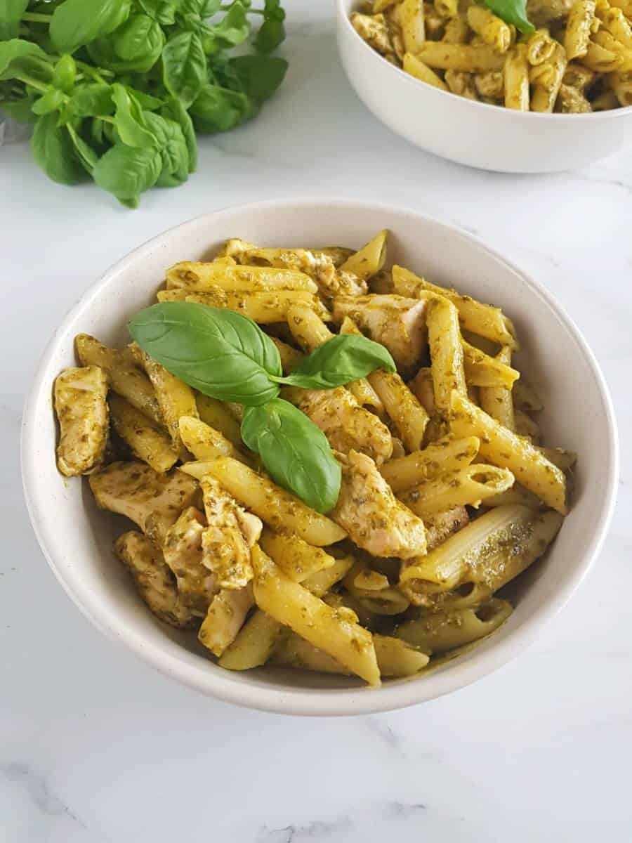 Pasta with chicken and pesto in a bowl on a marble table.