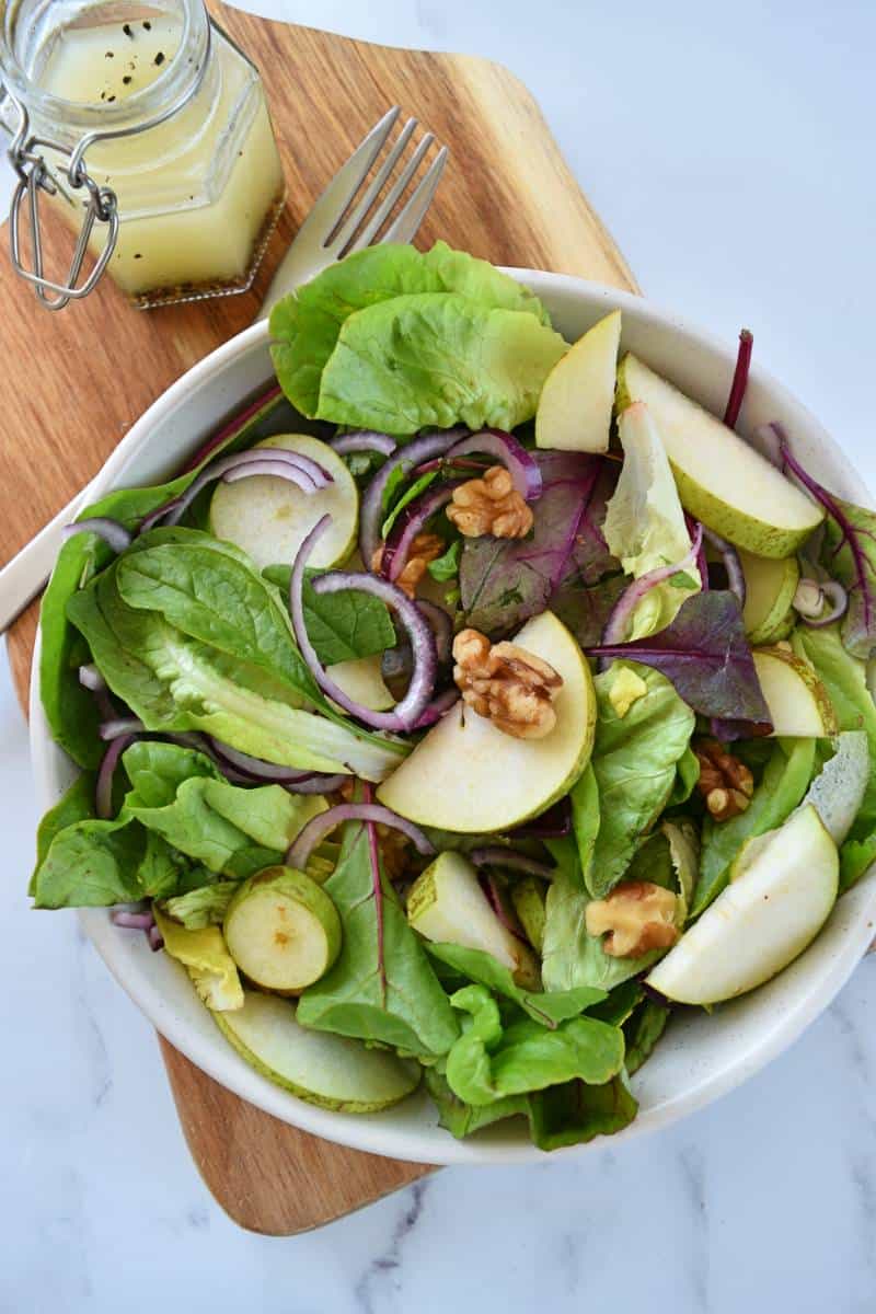 Pear and walnut salad in a bowl with dressing on the side.