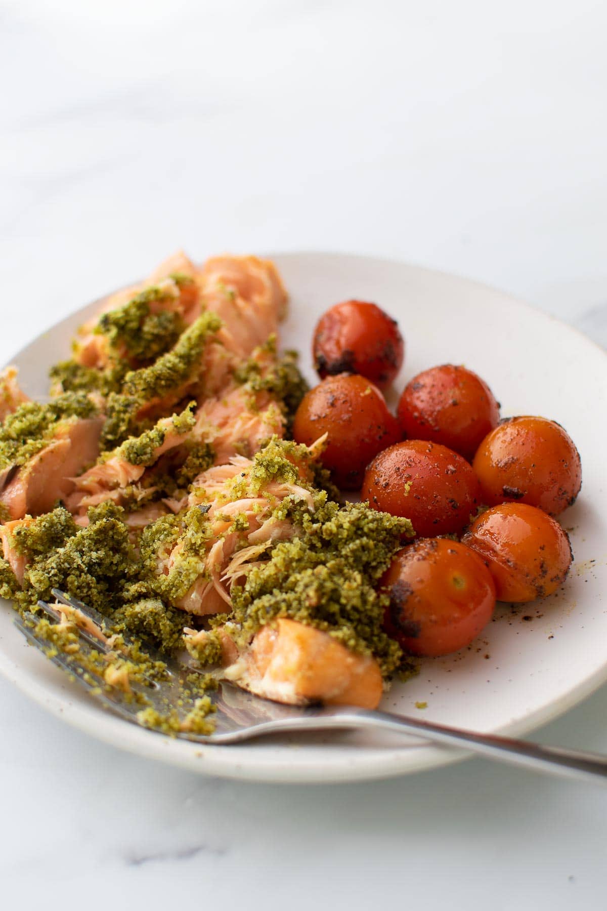 Smashed pesto crusted salmon on a plate with cherry tomatoes.