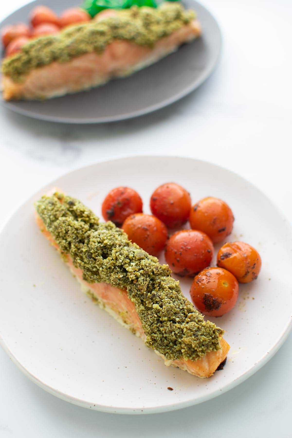 Pesto crusted salmon on a plate with cherry tomatoes on the side.