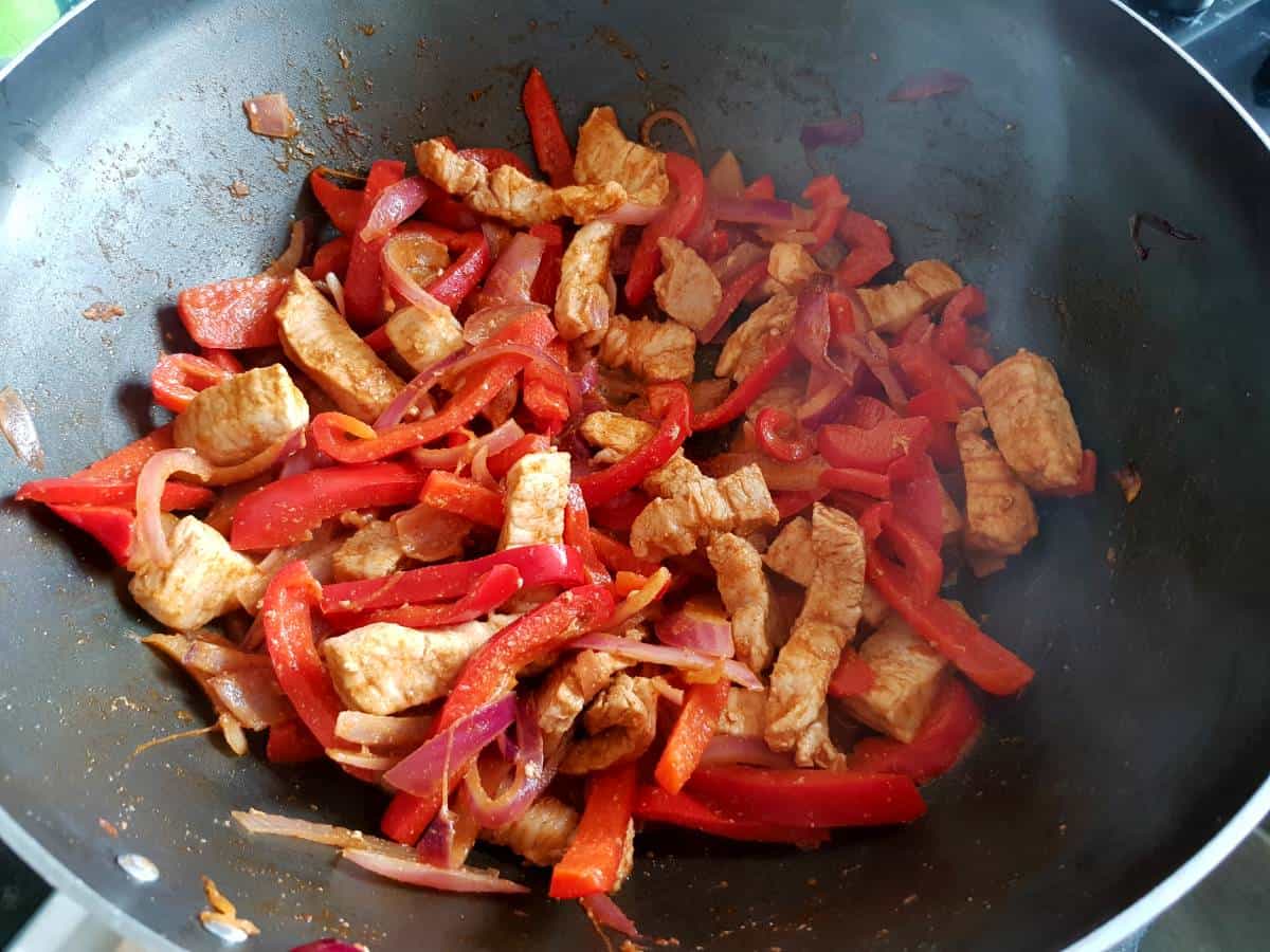 Pork fajitas cooking in a skillet.