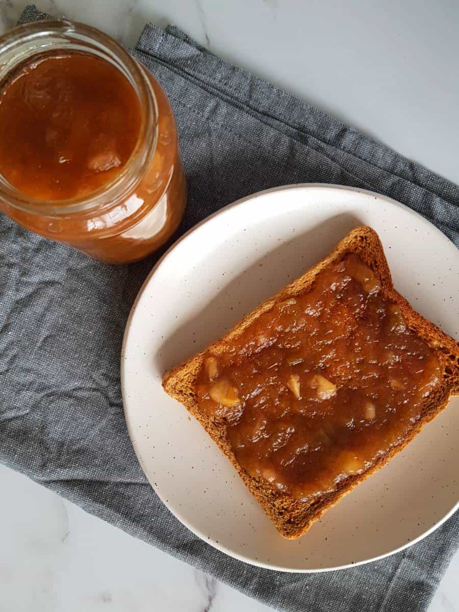 Rhubarb jam on a slice of toast, with a jar of jam in the background.