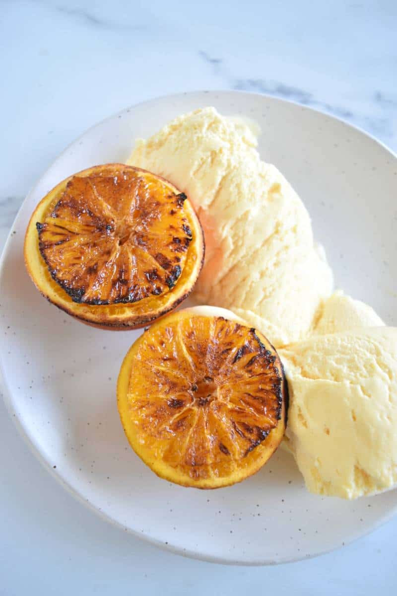 Roasted oranges on a plate with ice cream.