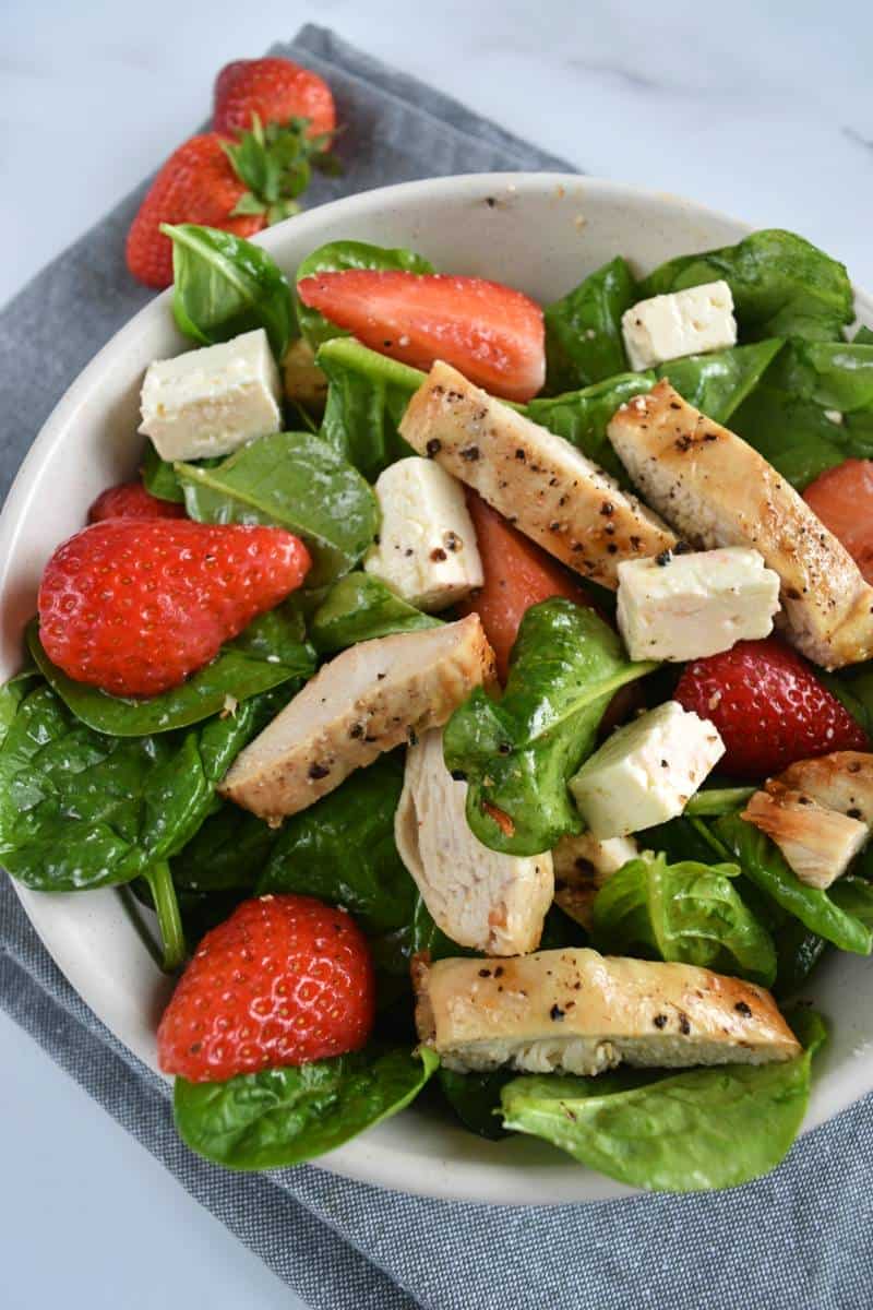 Salad with chicken feta and strawberries in a white bowl on a marble table.