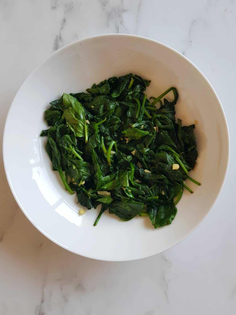 Sauteed spinach with garlic in a white bowl.