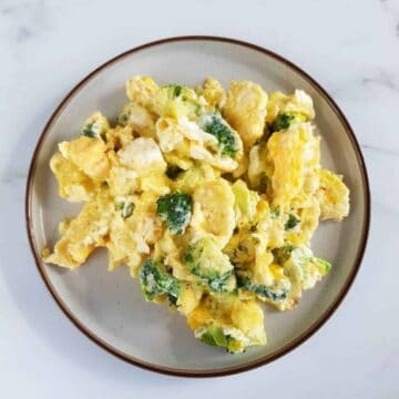 Scrambled eggs with cheese and broccoli on a plate on a marble table.