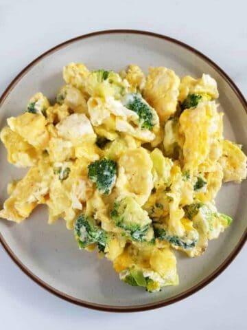 Scrambled eggs with cheese and broccoli on a plate on a marble table.