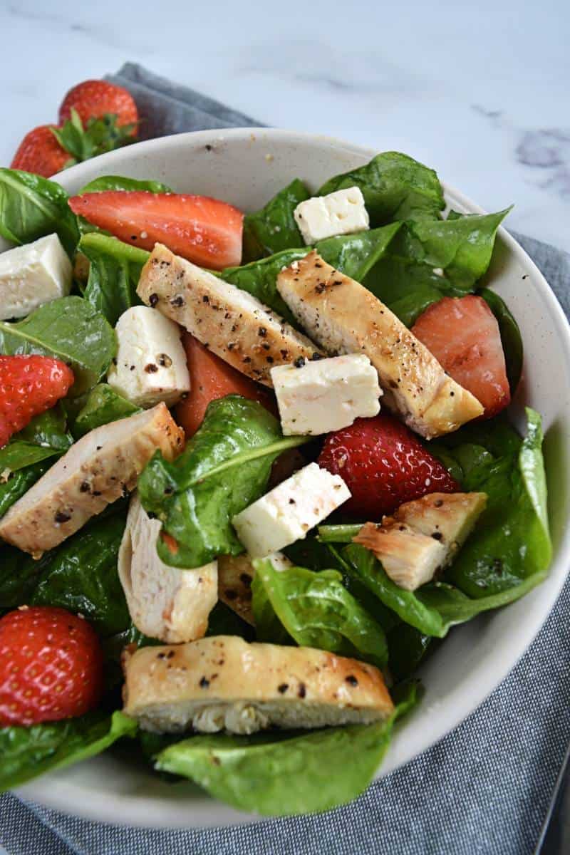 Spinach strawberry feta salad in a bowl with air fryer chicken.