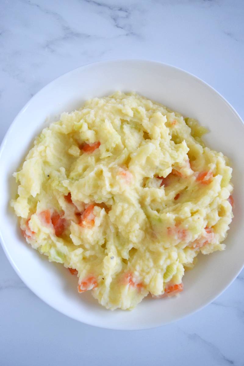 Stoemp with carrots and leek in a white bowl.