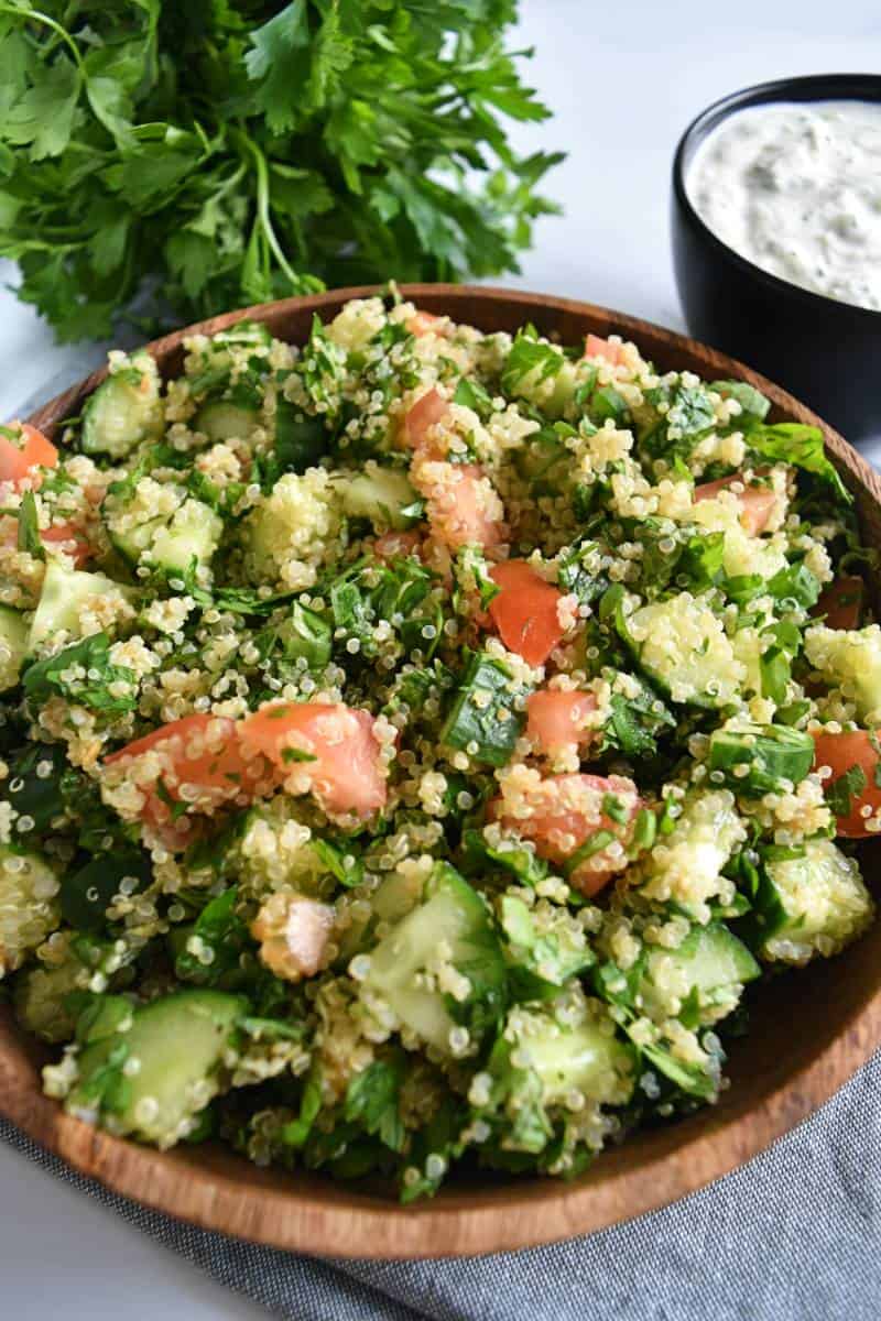 Tabbouleh with quinoa in a wooden bowl with fresh parsley in the background.