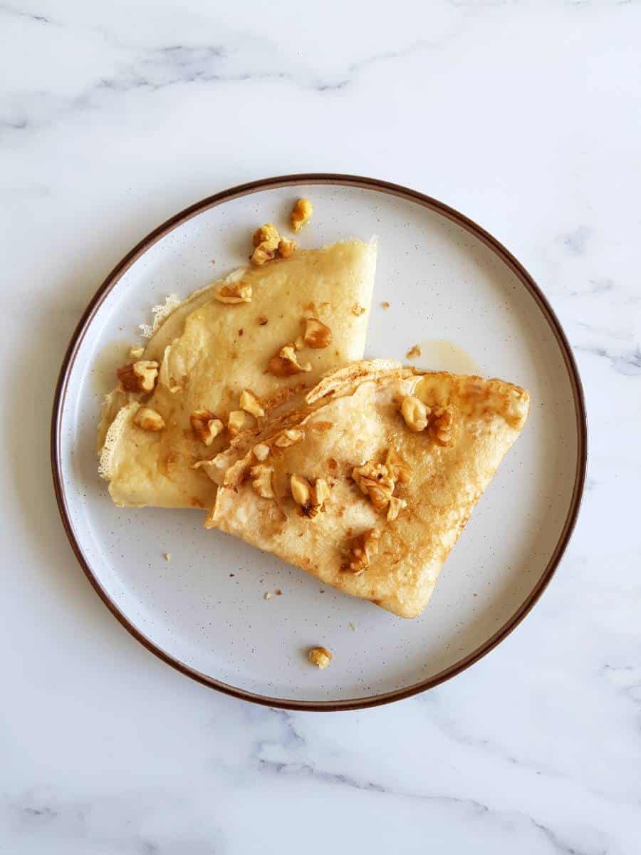 Two crepes on a plate on a marble table.