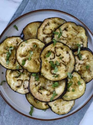 Za'atar roasted eggplant slices served on a plate with fresh herb garnish.