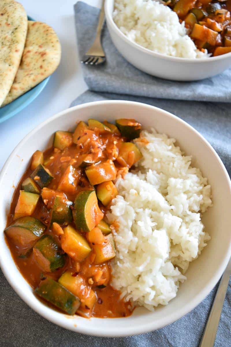 Zucchini curry in a white bowl with rice.