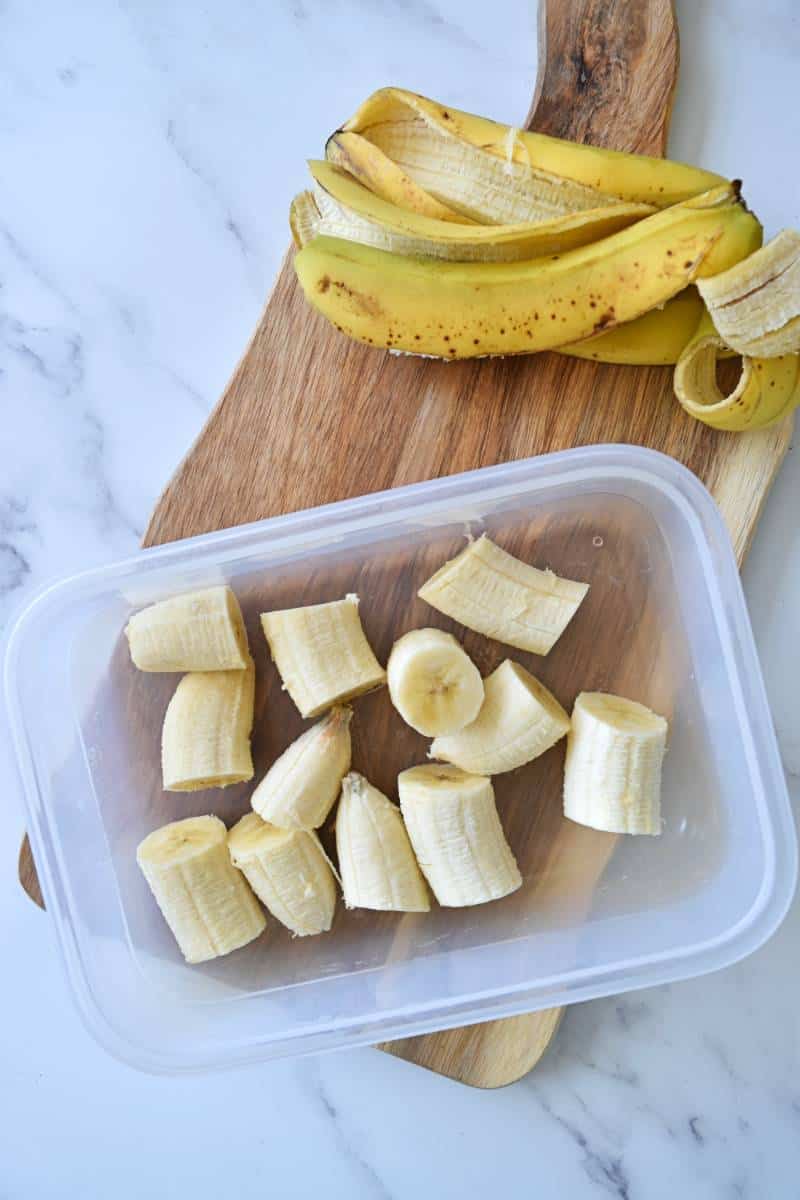 Diced bananas in a storage container with banana peels in the background.