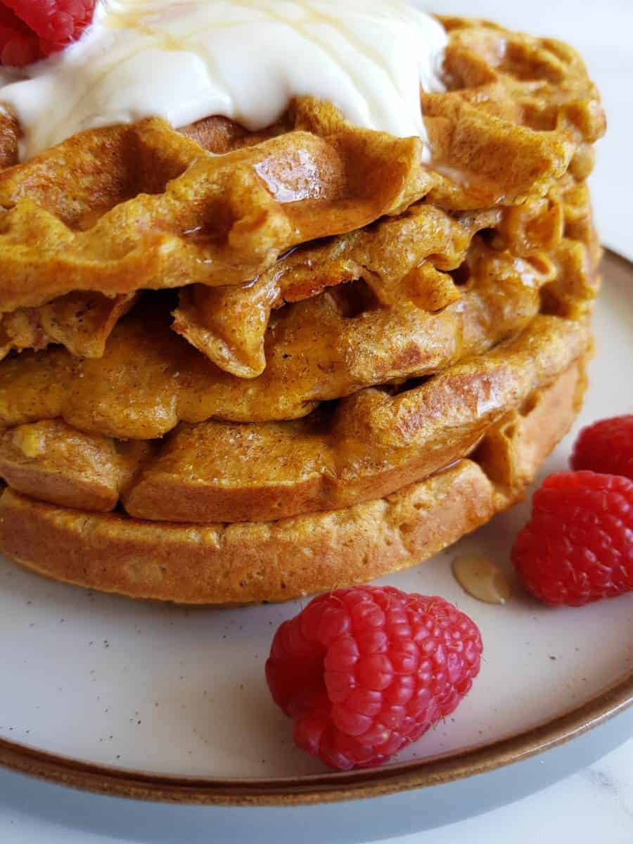 Butternut squash waffles on a plate with raspberries.