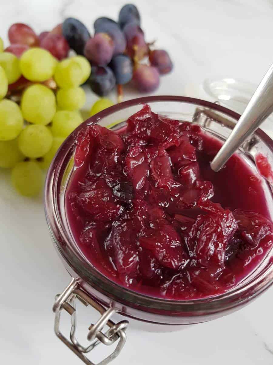 Grape jam in a jar with grapes in the background.
