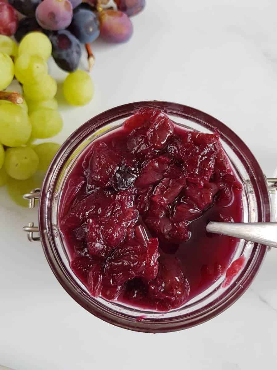 Grape jam with mixed grapes on a marble table.