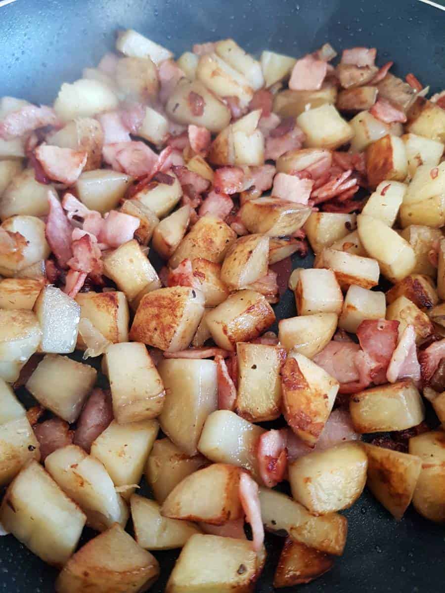 Pan fried potatoes and bacon in a skillet.