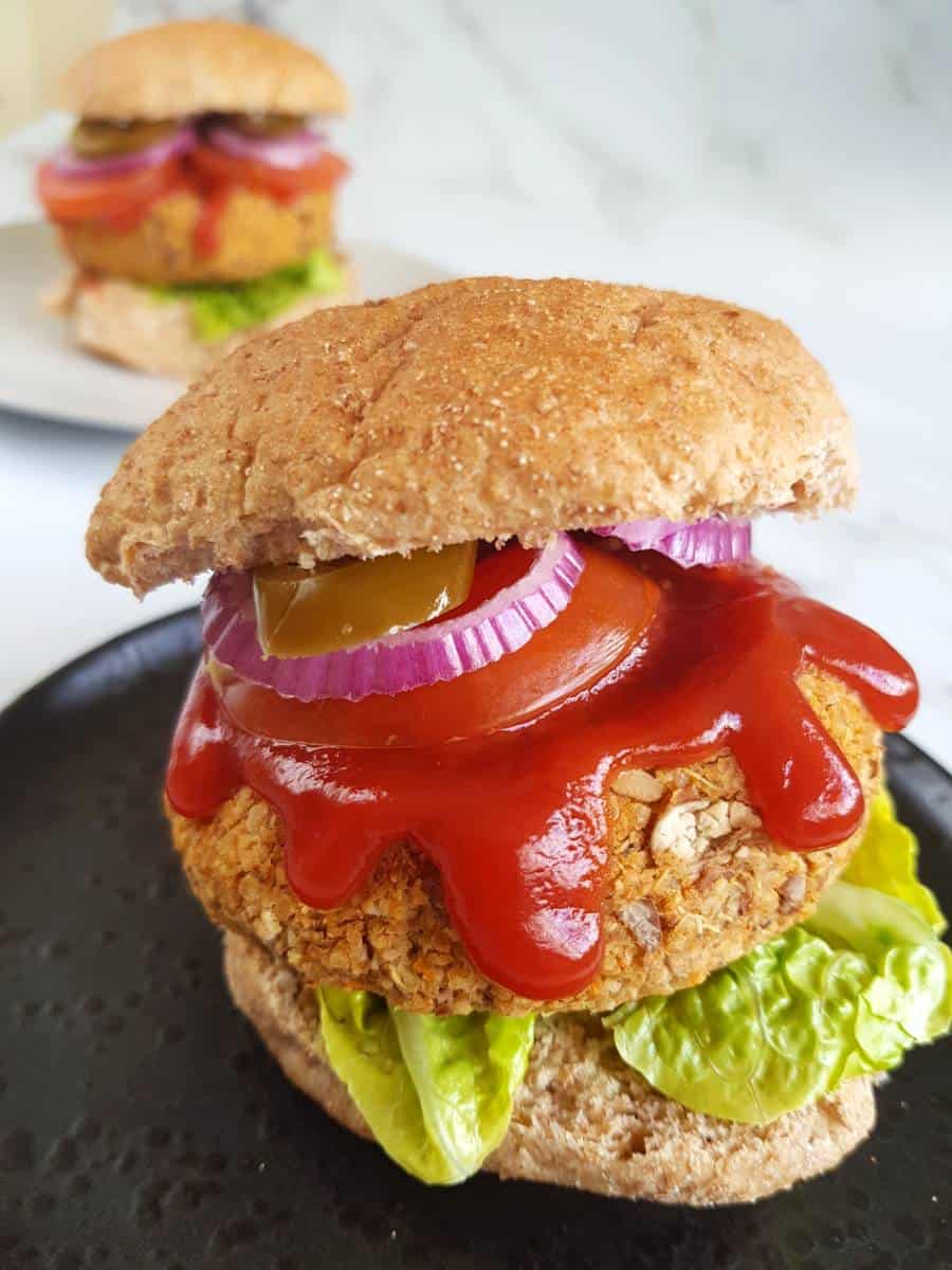 Pinto bean burger in a bun with lettuce, tomato, onions and ketchup.