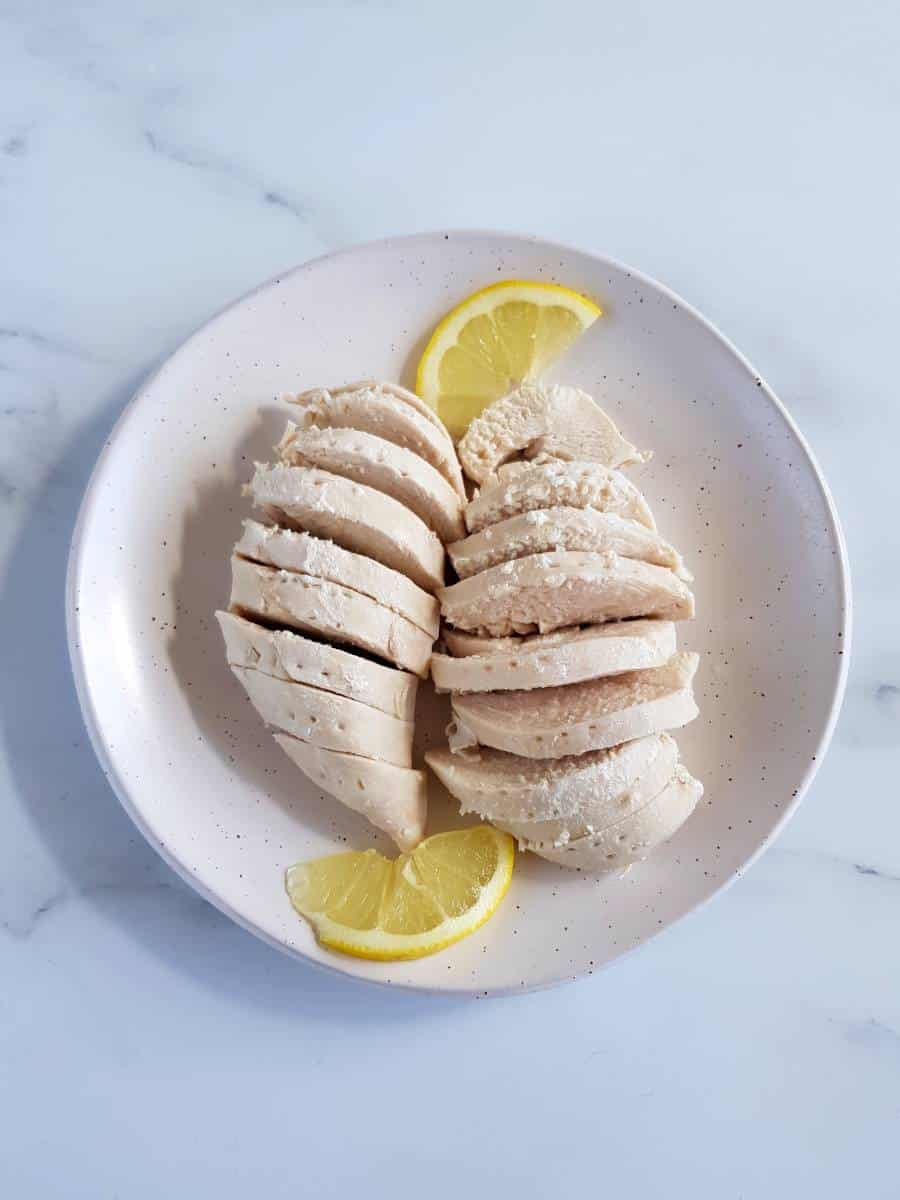 Poached chicken on a plate with lemon slices.