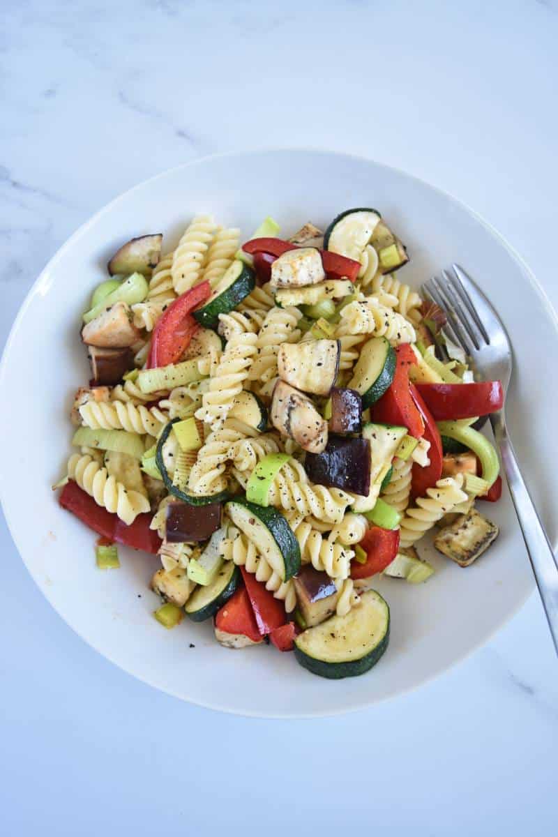 Roasted vegetables and pasta in a white bowl on a marble table.