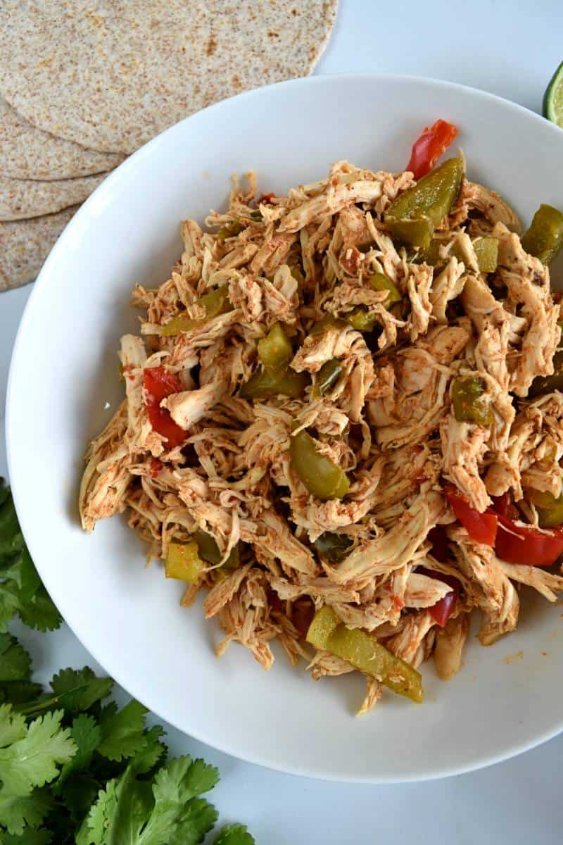 Shredded fajita chicken in a bowl with wraps, lime and cilantro.