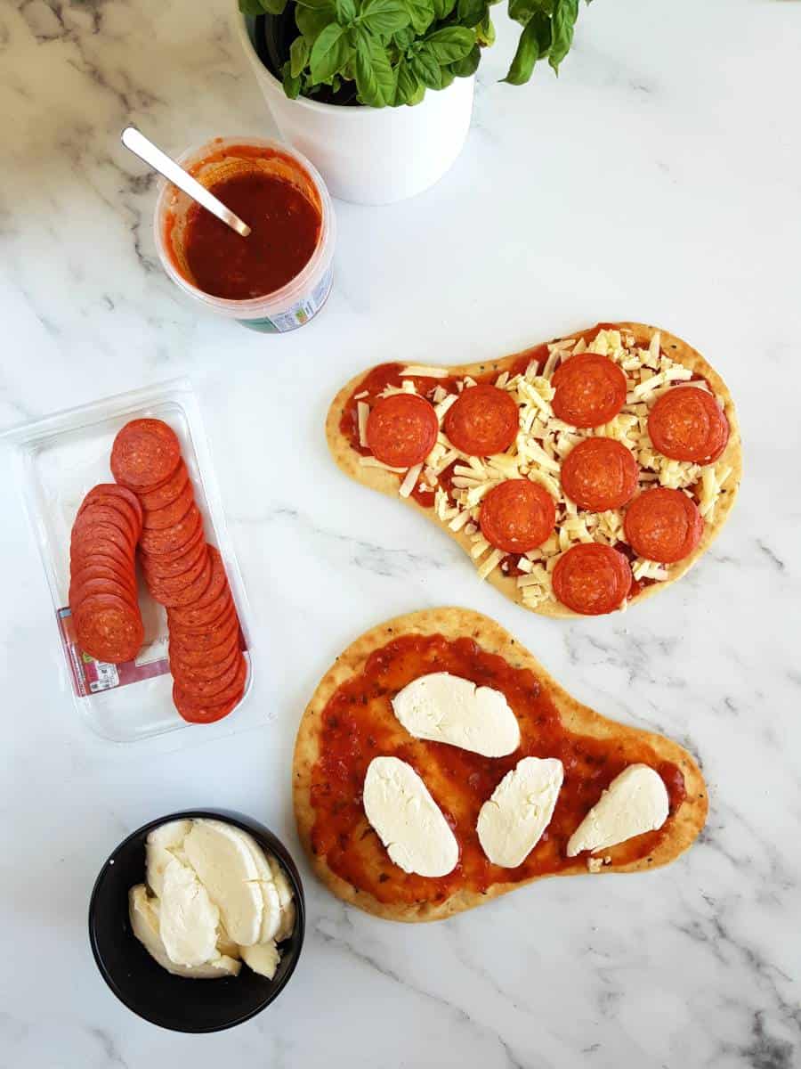 Uncooked naan pizzas on a marble table.