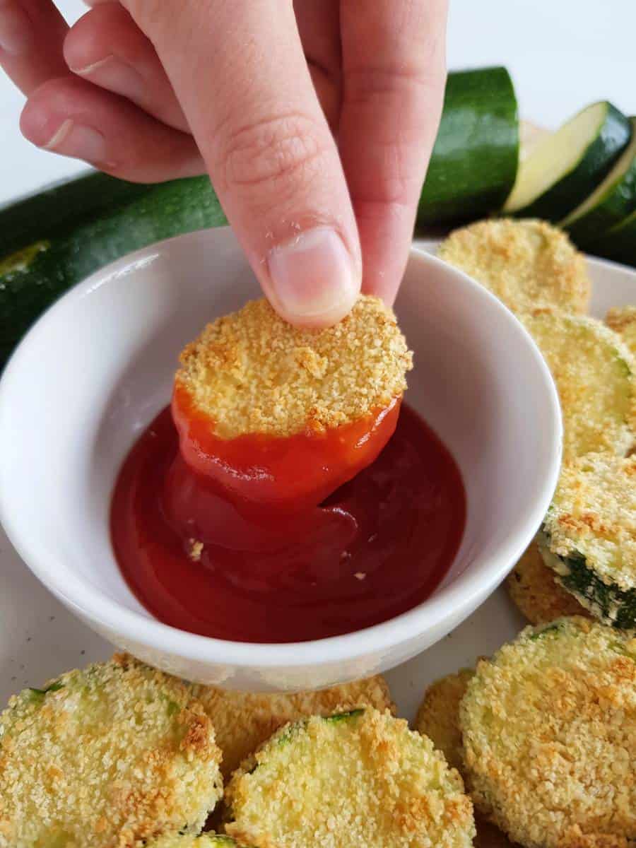 Zucchini chips being dipped into ketchup.