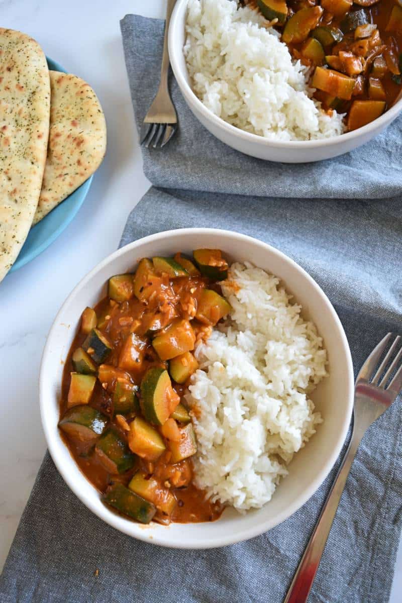 curry with zucchini in bowls with rice and naan bread.