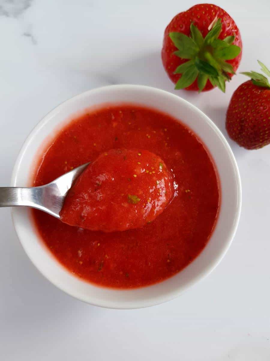 Strawberry basil sauce in a bowl with strawberries on the side.