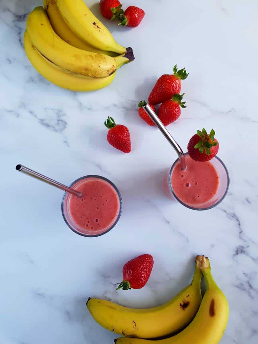 Strawberry smoothies on a table with strawberries and bananas.