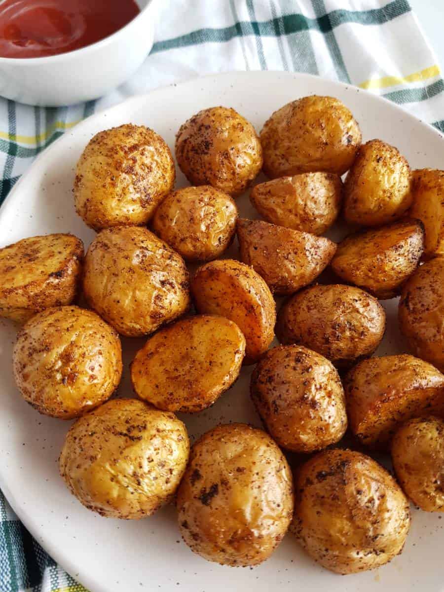 Air fryer roasted potatoes on a plate with ketchup in the back.