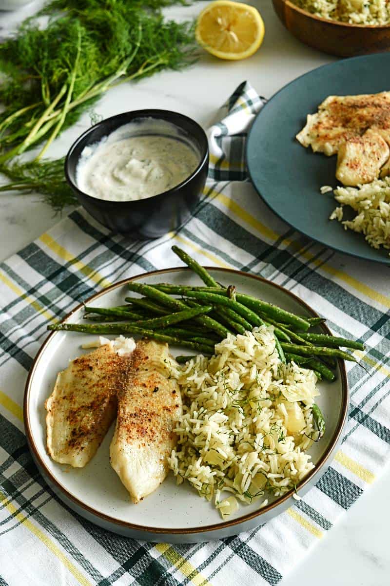 Tilapia with rice and green beans at a dinner table.